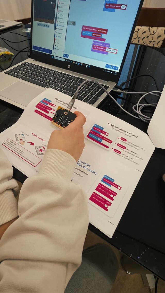 Dieťa drží micro:bit nad pracovným listom s návodom, malý počítač, ktorý celý projekt riadi