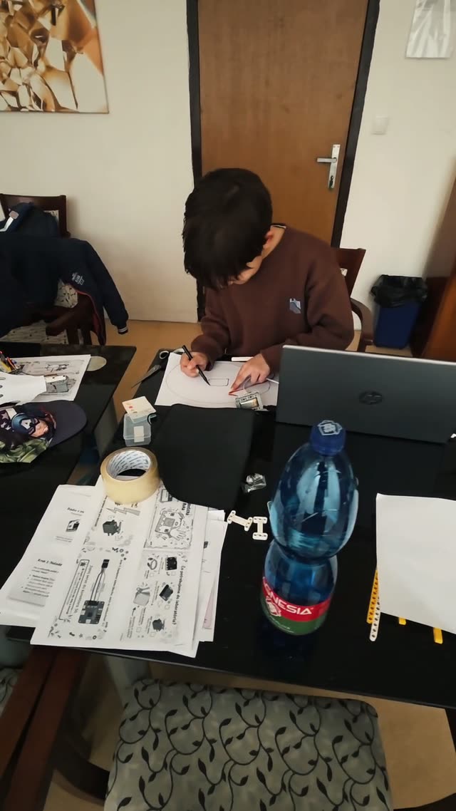 Dieťa si kreslí návrh projektu na papier vedľa notebooku, na krúžku sa začína nákresom a až potom sa stavia