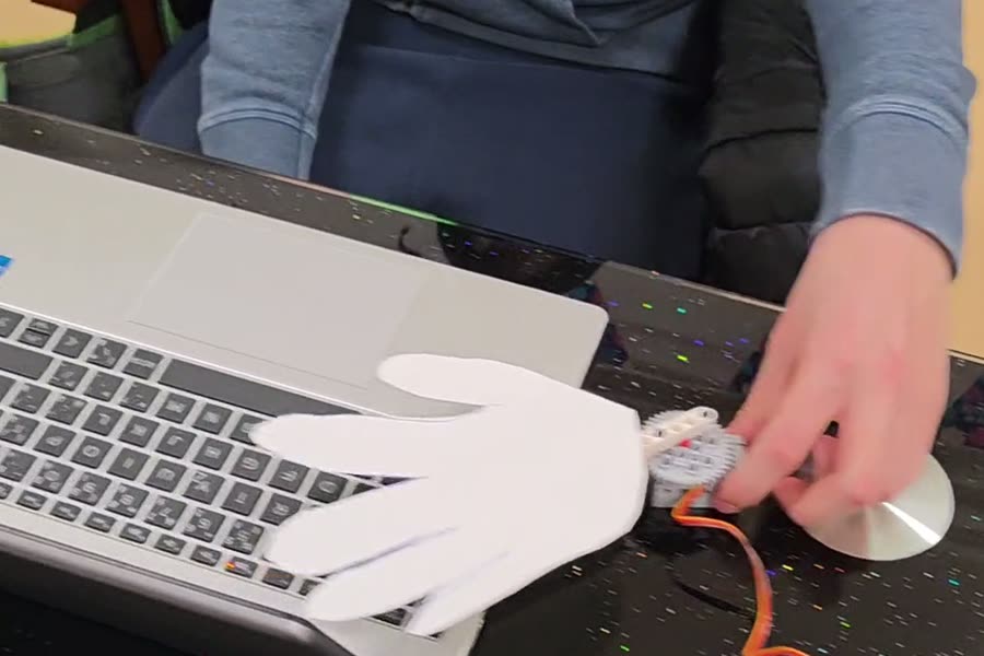 Papierová mávajúca ruka pripojená cez servo a micro:bit, položená pri notebooku